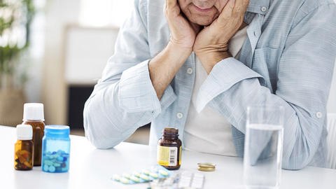 Mann schaut verzweifelt auf verschiedene Medikamente