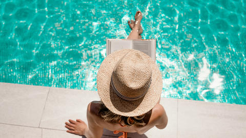 Frau liegt am Pool und liest